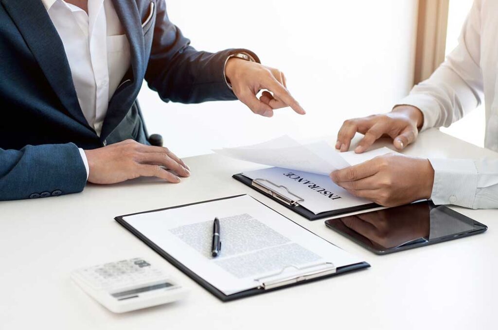 Young couple reviewing life insurance paperwork and household finances at a kitchen table.